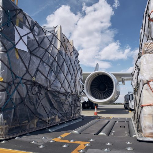 Preparation before flight. Loading of cargo containers against jet engine of freight airplane.